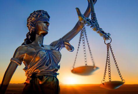 A statue of lady justice stands in front of a setting sun.